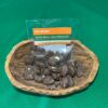 Bolsa de "Patas Muyu con Chocolate" de la marca Raíces del Napo, un snack artesanal de semillas de macambo tostadas cubiertas con chocolate negro, presentado en un recipiente rústico sobre un fondo verde.